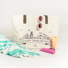 Cargar imagen en el visor de la galería, Bolso con skyline de Alicante con estampado “La millor terreta del món”, asas de cinta tejida en beige y negro.
