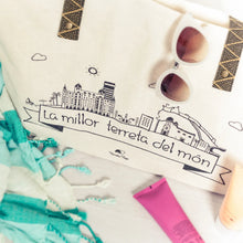 Cargar imagen en el visor de la galería, Bolso tote de tela color crudo con ilustración de Alicante y el texto “La millor terreta del món”, asa de cinta tejida negra y beige
