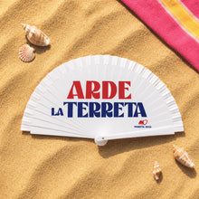 Cargar imagen en el visor de la galería, Abanico blanco abierto con diseño “Arde la Terreta” en naranja y azul del paseo de Alicante sobre arena de playa luminosa
